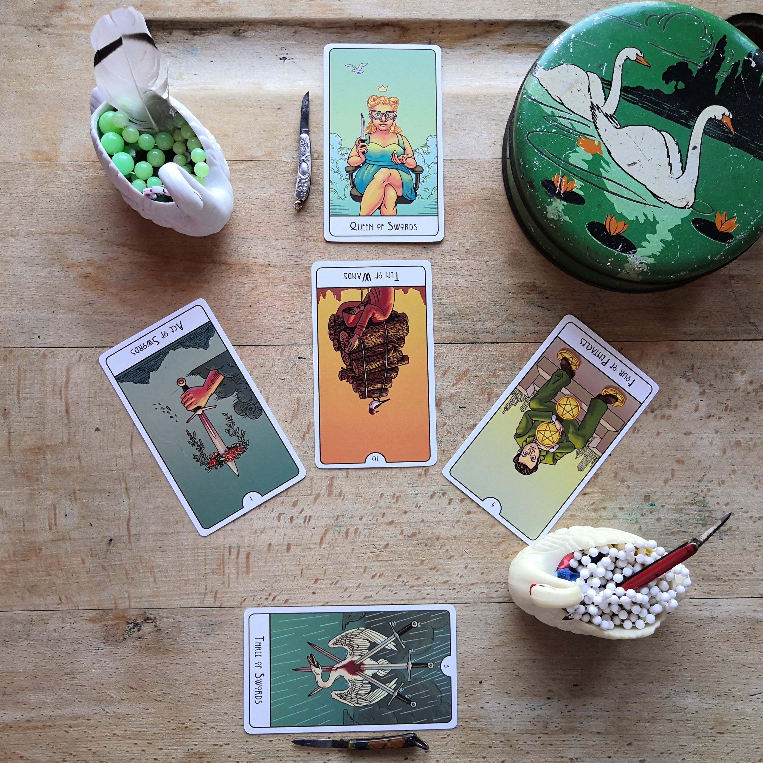 a tarot spread with This Might Hurt Tarot, some vintage swan figurines, box and tiny knives